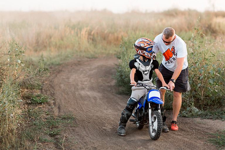 Homem ajuda criança a andar de moto na estrada de terra